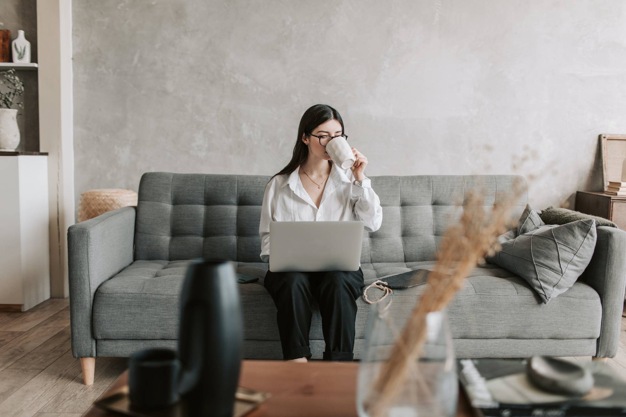 Woman on sofa drinking a coffee and working on a computer