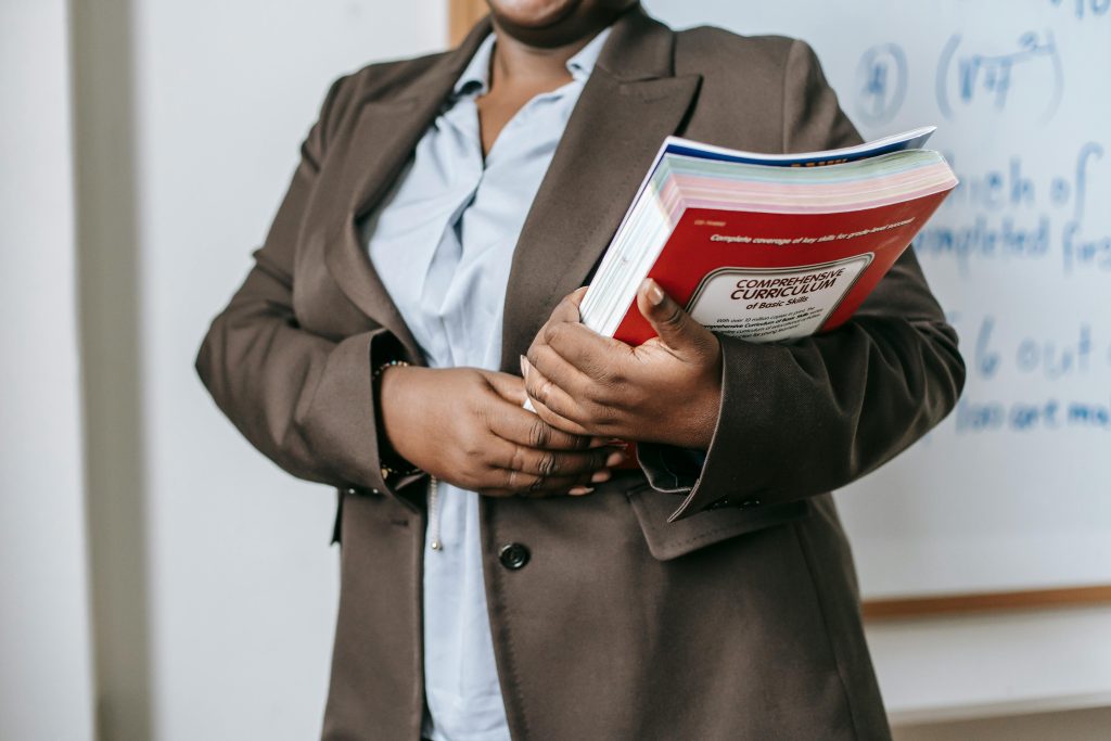 female educator with books standing near whiteboard at school