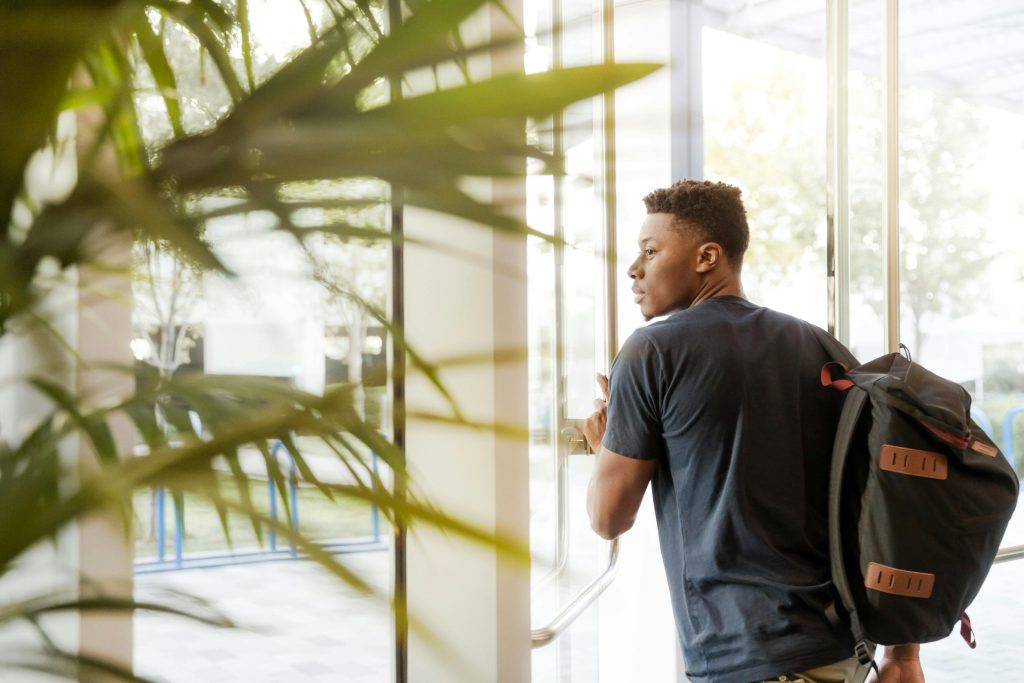 Man Walking Out Of A Door Carrying Black and Brown Backpack