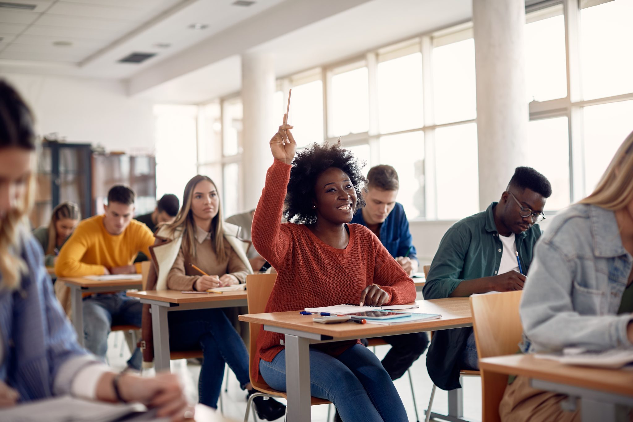 Student raising her hand to ask a question during lecture in the classroom.