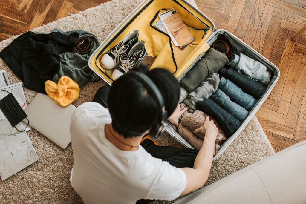 A Man Listening on His Headphones while Packing His Clothes.