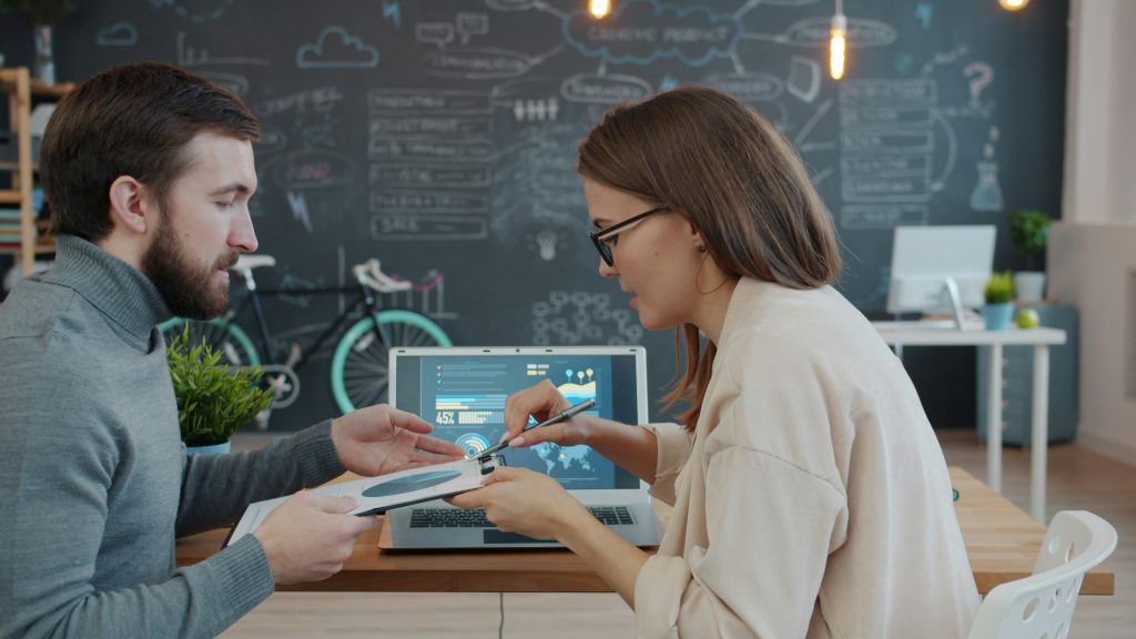 Man and woman colleagues are discussing business looking at laptop screen in modern office